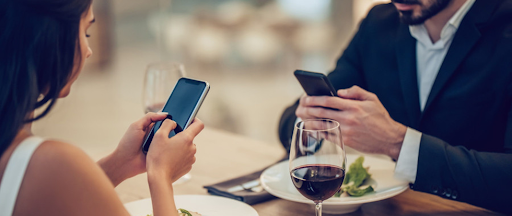 Un couple en train de diner dans un restaurant et utilisant chacun leur smartphone