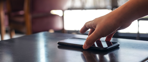 Une main en train de prendre son smartphone posé sur la table